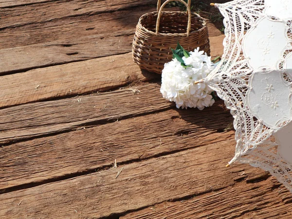 木地板上的白色假绣花花花束 柳条藤篮和雨伞 — 图库照片