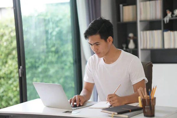 Asyalı genç öğrenci genç girişimci bilgisayar yazma notuyla çalışıyor evde internetten öğrenim görüyor. Webinar toplantısını öğreniyorum. Covid salgınında sosyal uzaklık