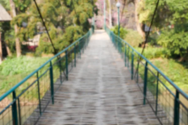 Blurry defocused image of wooden suspension bridge across the ri — Stock Photo, Image