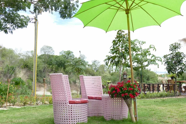 Sofá de mimbre rosa con paraguas verde en el jardín — Foto de Stock