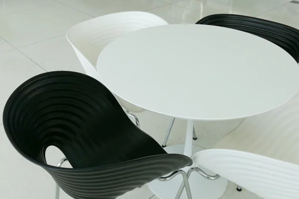 Svart och vit plast stol med vita runda skrivbord — Stockfoto