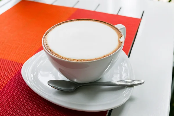 Ζεστό καπουτσίνο στο λευκό κεραμικό Κύπελλο στο λευκό ξύλινο τραπέζι — Φωτογραφία Αρχείου
