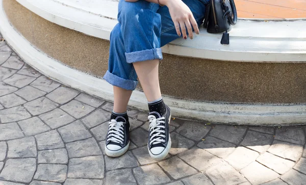 Chica vistiendo jeans y zapatilla de deporte sentado y esperando — Foto de Stock