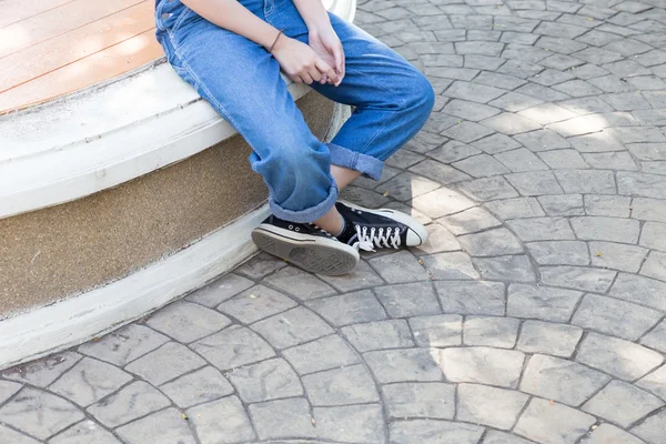 Chica vistiendo jeans y zapatilla de deporte sentado y esperando — Foto de Stock