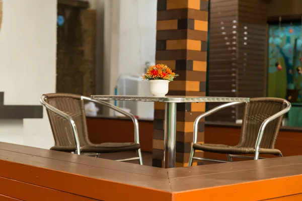 Fleur orange sur table en métal avec chaise en osier — Photo