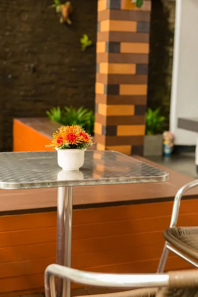 Оранжевый цветок на металлическом столе с плетеным стулом — стоковое фото