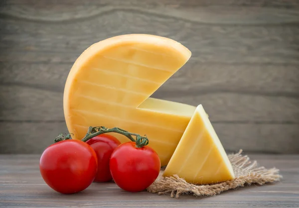 Smoked cheese wheel, tomatoes on wooden table — Stock Photo, Image