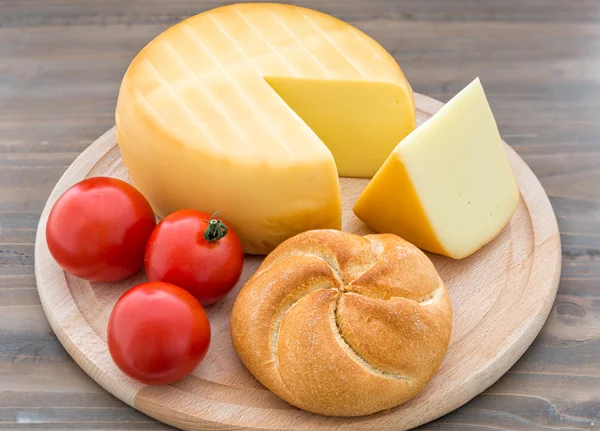 Roda de queijo defumado, tomates e pão na mesa de madeira — Fotografia de Stock