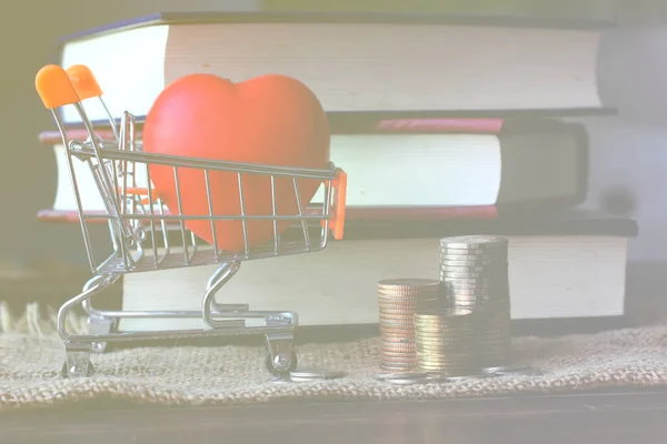 coins stacking red heart on shopping cart with books background.  love and invest in education for future , education concept