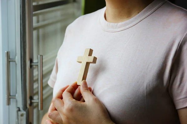 Christian woman holding a wooden cross against her chest while praying God protect