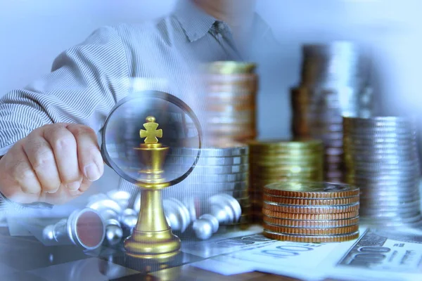 İş adamı büyüteç kullanarak altın kral satrancı banknotlara para istifliyor, iş konsepti