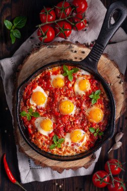Domates ve sebzeli sahanda yumurta. Shakshuka, ahşap arka plan manzaralı dökme demir bir tavada. Geleneksel kahvaltı yemeği.