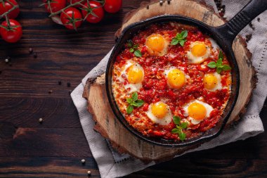 Domates ve sebzeli sahanda yumurta. Shakshuka, ahşap arka plan manzaralı dökme demir bir tavada. Geleneksel kahvaltı yemeği.