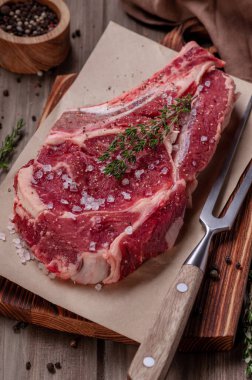 Çiğ pişmemiş biftek. Kemiğin üzerinde büyük bir parça et, baharatlar ve taze otlarla birlikte ahşap bir tahtanın üzerinde yatıyor. Pişirmeye hazır. Etobur ya da ketojenik diyet.