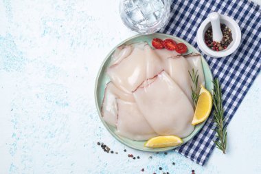 Limonlu, domatesli ve biberiyeli taze çiğ kalamar filetosu. Mürekkep balığının büyük bir kısmı yemek pişirmek için hazırlanır. Mavi arkaplanda üst görünüm. 