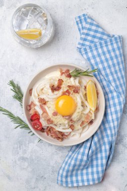 Kızarmış domuz pastırması, parmesan peyniri ve yumurta sarısı ile klasik carbonara makarnası. Carbonara soslu karbonhidratsız shirataki makarnası. Mavi arkaplanda beyaz bir tabakta büyük bir porsiyon.