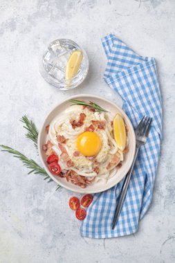 Kızarmış domuz pastırması, parmesan peyniri ve yumurta sarısı ile klasik carbonara makarnası. Carbonara soslu karbonhidratsız shirataki makarnası. Mavi arkaplanda beyaz bir tabakta büyük bir porsiyon.