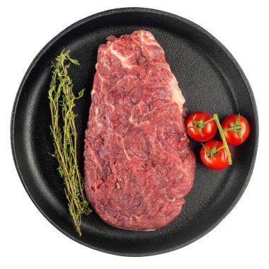 Taze sebzeli çiğ biftek, domates, otlar ve baharatlar beyaz arka planda izole edilmiş dökme demir bir tavada. Üst görünüm.