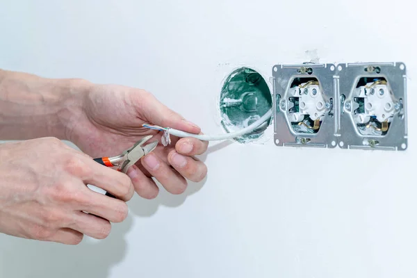 The craftsman installs an electrical outlet into the wall. Mounting the outlet in compliance with safety precautions. Close-up. Selective focus.