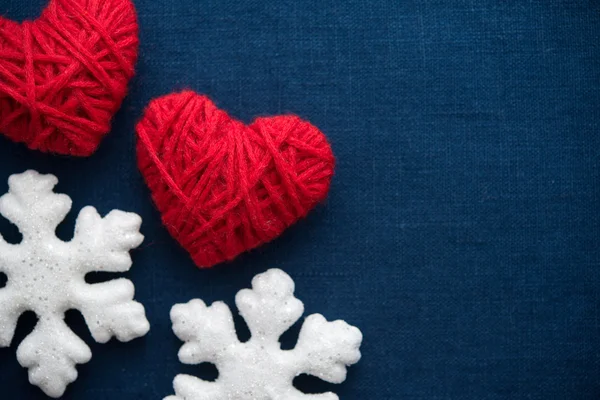 White snowflakes and red wool hearts on blue canvas background. Merry christmas card. Winter holidays. Xmas theme. Happy New Year. — Stock Photo, Image
