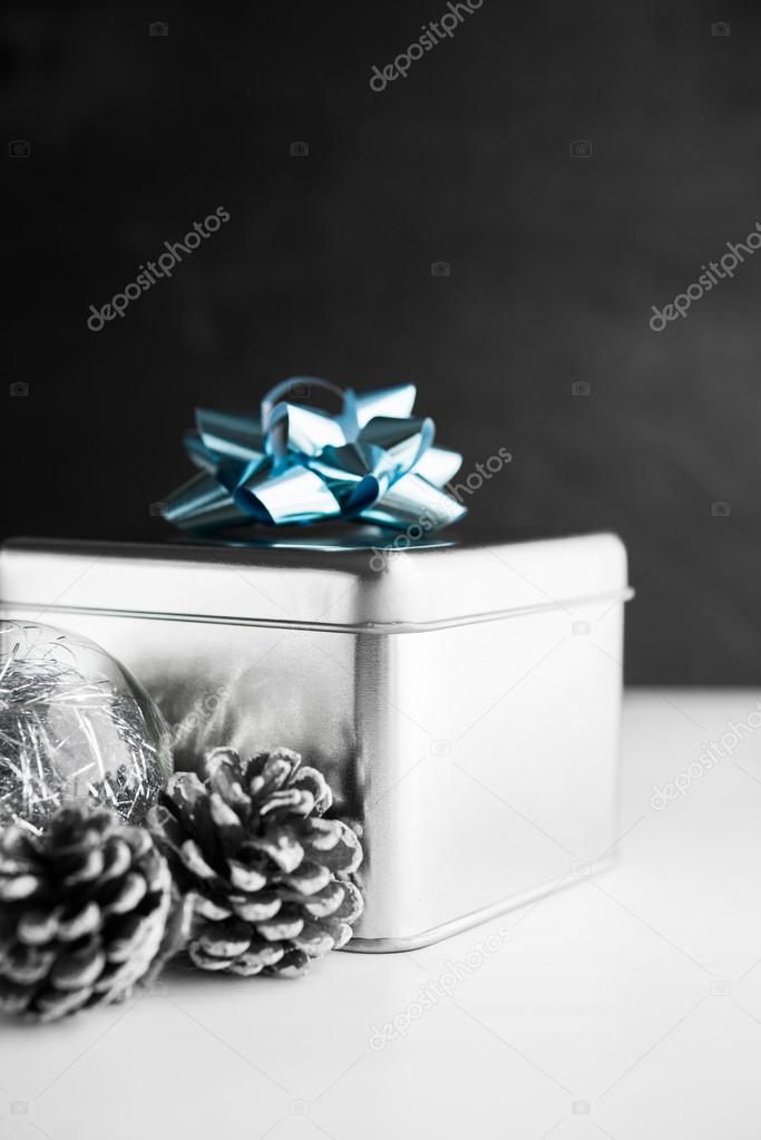 Metal gift box with blue bow and xmas baubles on white and black wooden backgrounds. Merry christmas card. Winter holidays. Xmas theme. Happy New Year.