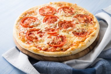 Mavi ahşap arka planda domatesli, peynirli ve kuru fesleğenli pizza. İtalyan mutfağı.