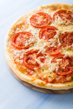 Mavi ahşap arka planda domatesli, peynirli ve kuru fesleğenli pizza. İtalyan mutfağı.