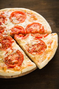 Koyu ahşap arka plan üzerinde domates, peynir ve kuru fesleğen ile dilimlenmiş pizza yakın. İtalyan mutfağı.