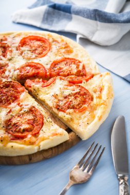 Mavi ahşap arka plan üzerinde domates, peynir ve kuru fesleğen ile dilimlenmiş pizza yakın. İtalyan mutfağı.