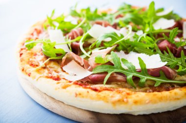 Pizza prosciutto ile (parma jambon), arugula (salata roket) ve parmesan mavi ahşap arka plan yakın. İtalyan mutfağı.