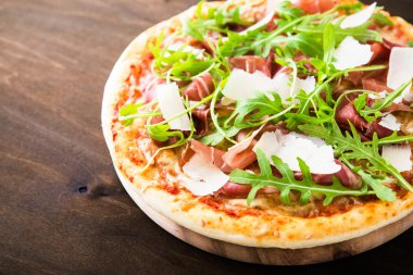 Pizza prosciutto ile (parma jambon), arugula (salata roket) ve parmesan koyu ahşap arka plan yakın. İtalyan mutfağı.