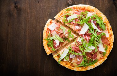 Prosciutto (parma jambon), arugula (salata roket) ve parmesan koyu ahşap arka plan üst görünümü nde dilimlenmiş pizza. İtalyan mutfağı.