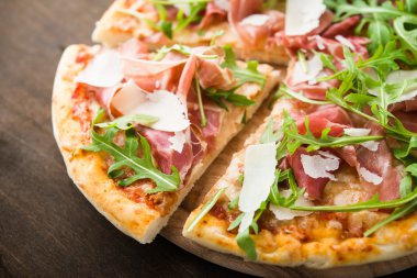 Prosciutto ile Dilimlenmiş pizza (parma jambon), arugula (salata roket) ve parmesan koyu ahşap arka plan yakın. İtalyan mutfağı.