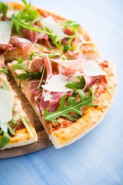Prosciutto ile dilimlenmiş pizza (parma jambon), arugula (salata roket) ve parmesan mavi ahşap arka plan yakın. İtalyan mutfağı.