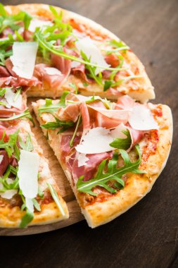 Prosciutto ile Dilimlenmiş pizza (parma jambon), arugula (salata roket) ve parmesan koyu ahşap arka plan yakın. İtalyan mutfağı.