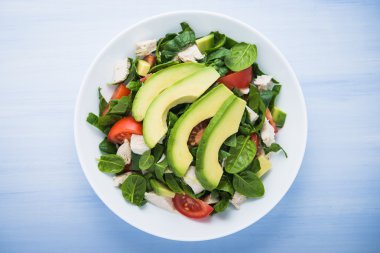 Taze salata tavuk, domates, ıspanak ve mavi ahşap arka plan üstten görünüm üzerinde avokado. Sağlıklı gıda.
