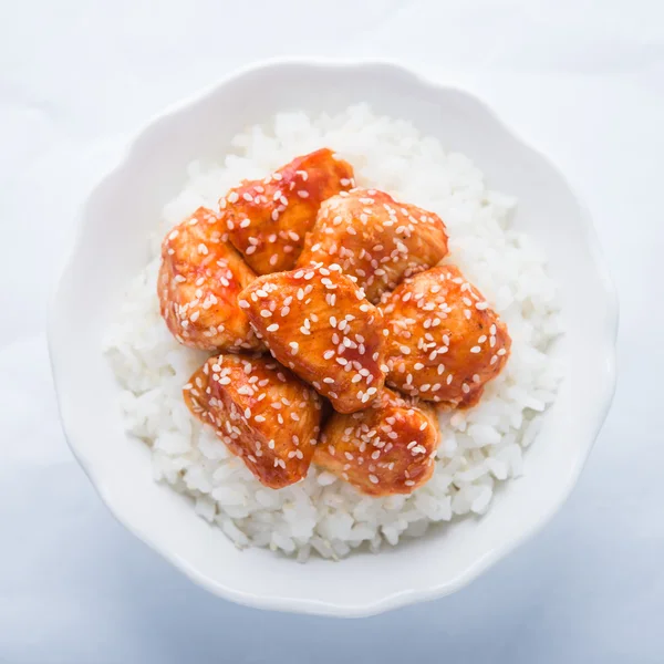 Spicy sweet and sour chicken with sesame and rice on white background top view. Oriental food.