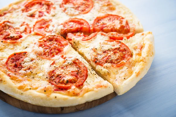 Pizza affettata con pomodoro, formaggio e basilico secco su fondo blu in legno da vicino. Cucina italiana . — Foto Stock