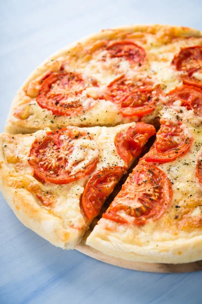 Pizza affettata con pomodoro, formaggio e basilico secco su fondo blu in legno da vicino. Cucina italiana . — Foto Stock