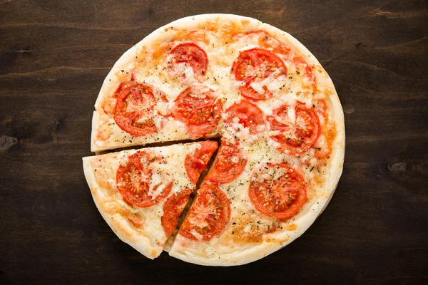 Pizza affettata con pomodoro, formaggio e basilico secco su fondo in legno scuro vista dall'alto. Cucina italiana . — Foto Stock