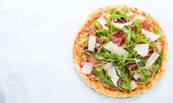 Pizza with prosciutto (parma ham), arugula (salad rocket) and parmesan on white background top view. Italian cuisine. Space for text.