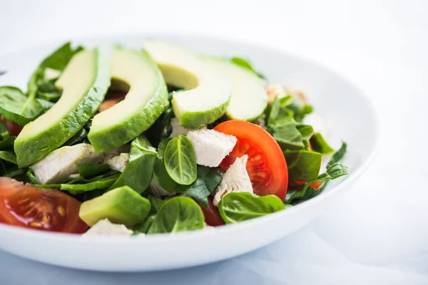 Fresh salad with chicken, tomatoes, spinach and avocado on white background close up. Healthy food.