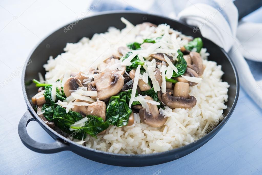 Rice (risotto) with mushrooms, parmesan and spinach close up on blue wooden background. Italian cuisine.