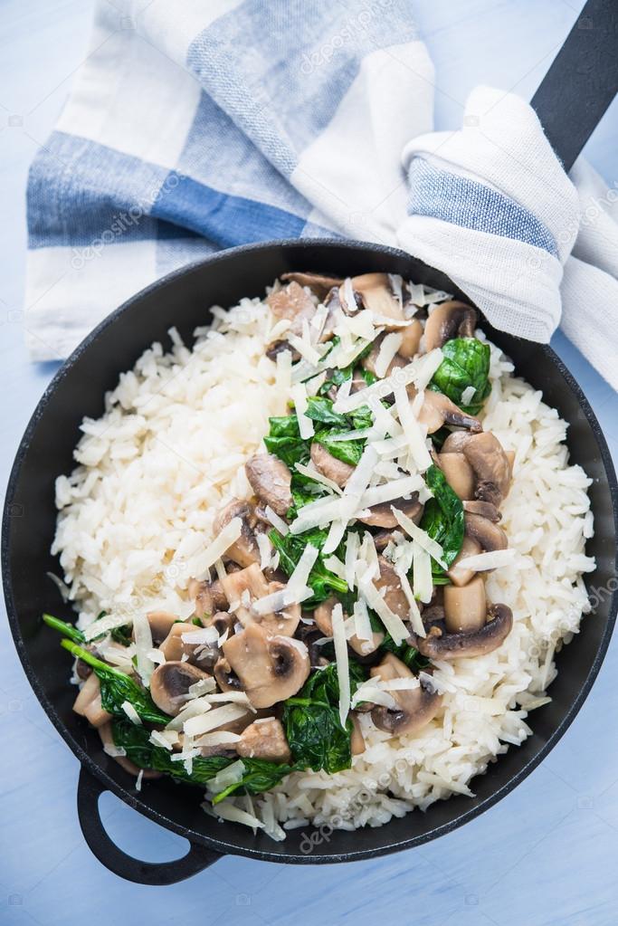Rice (risotto) with mushrooms, parmesan and spinach top view on blue wooden background. Italian cuisine.