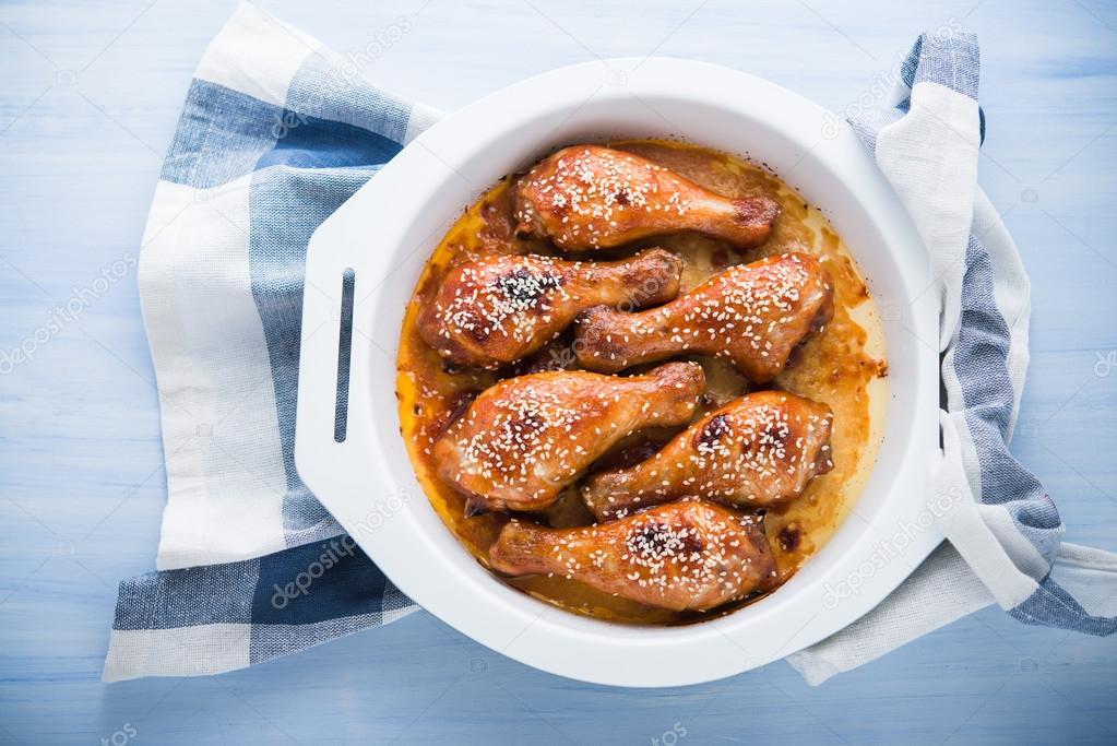 Baked spicy chicken legs with sesame on blue wooden background top view.