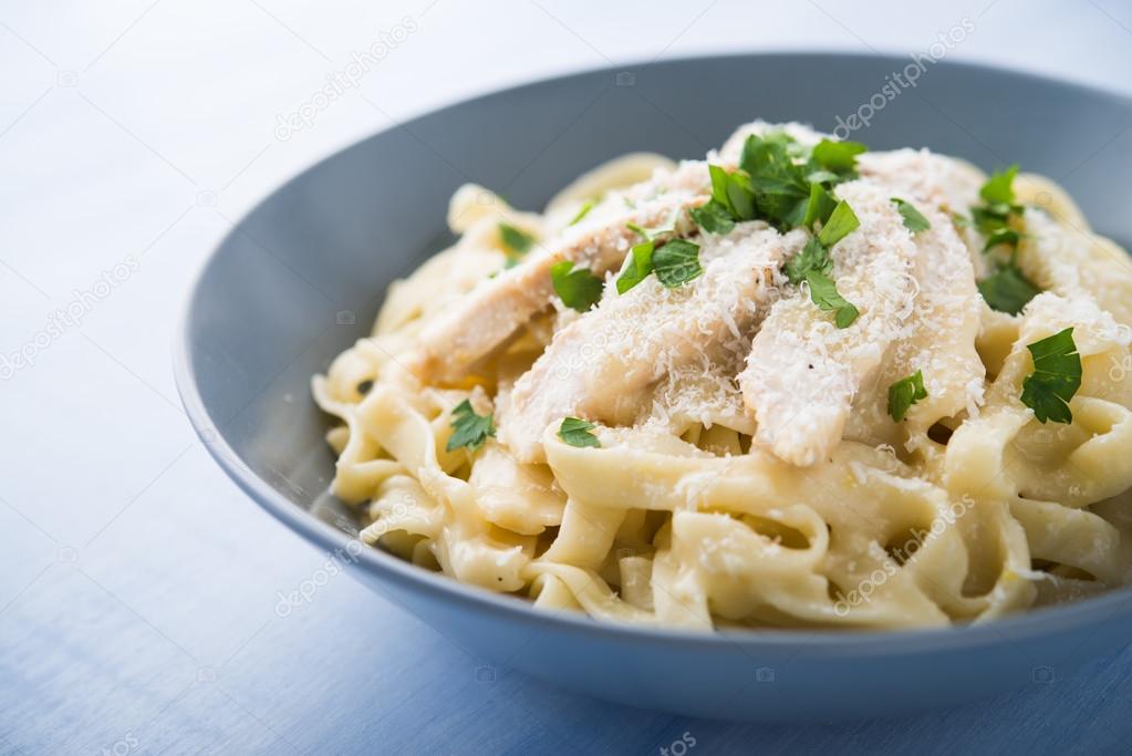 Pasta fettuccine alfredo with chicken, parmesan and parsley on blue wood background close up. Italian cuisine.