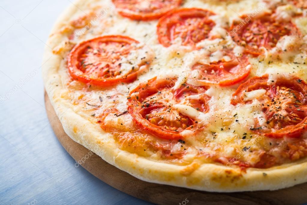 Pizza with tomato, cheese and dry basil on blue wooden background close up. Italian cuisine.