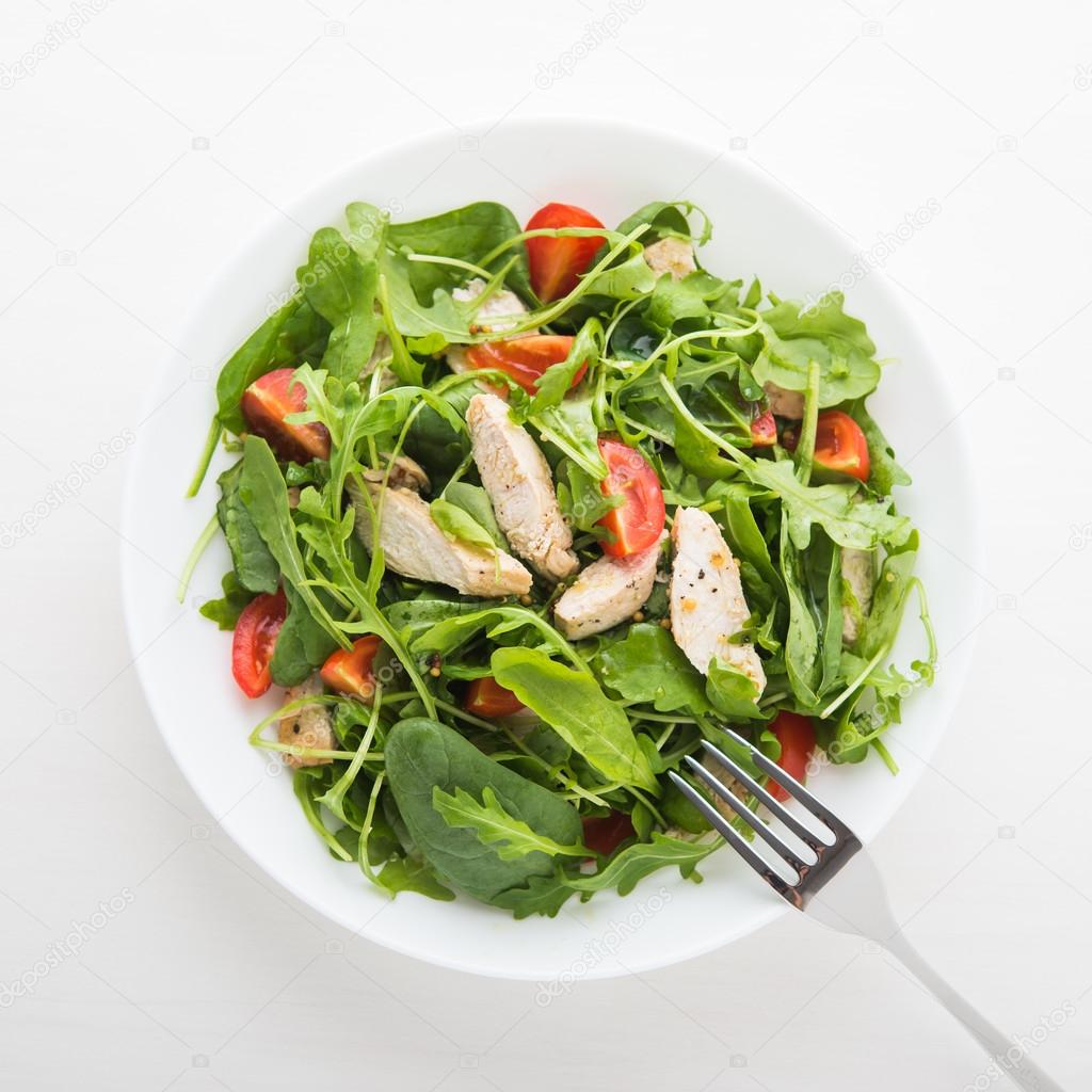 Fresh salad with chicken, tomato and greens (spinach, arugula) on white background top view. Healthy food.