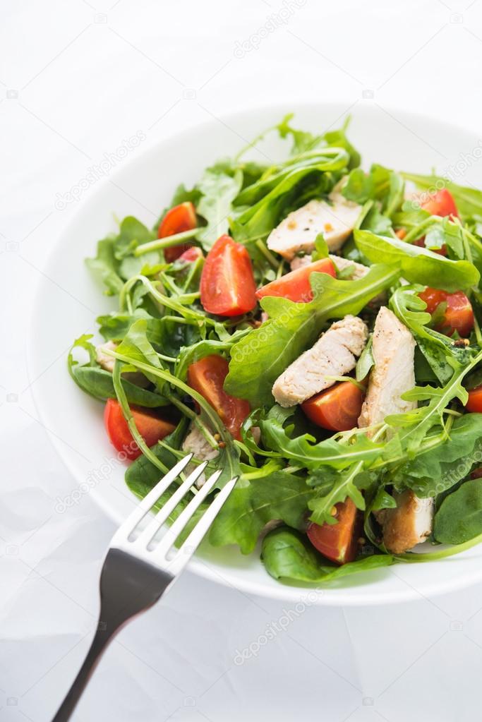 Fresh salad with chicken, tomato and greens (spinach, arugula) on white background close up. Healthy food.