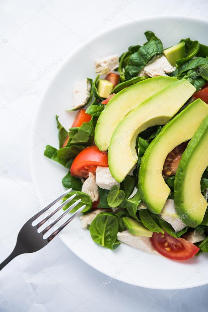 Fresh salad with chicken, tomatoes, spinach and avocado on white background top view. Healthy food.